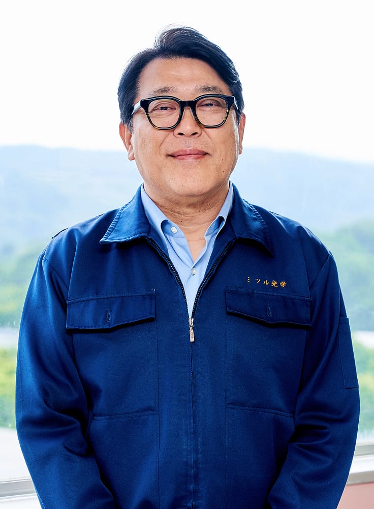青い作業服を着て微笑む代表取締役社長の山邉 英彦