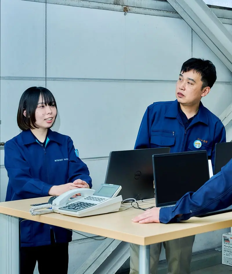 ノートパソコンや電話が載っている机を囲み話をしている従業員たち