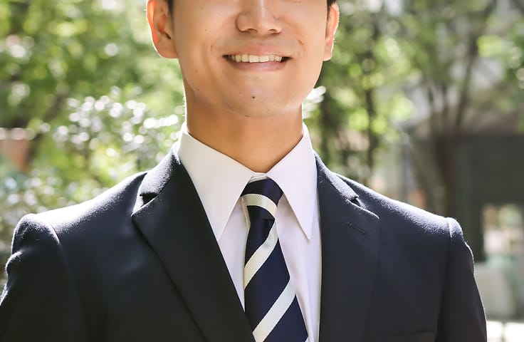 明るい屋外で微笑んでいるスーツを着た男性