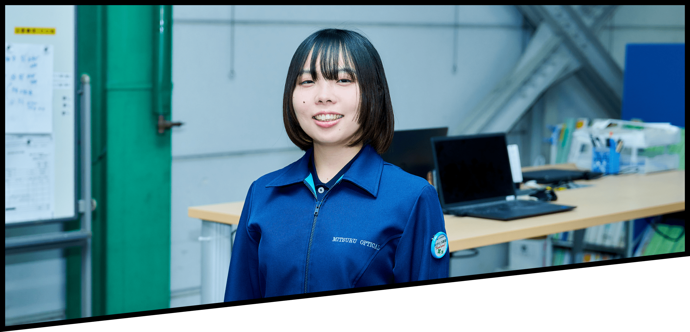 ノートパソコンが並ぶ机の前で微笑む2019年入社の女性社員