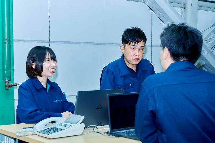 ノートパソコンや電話が載っている机を囲み話をしている従業員3人